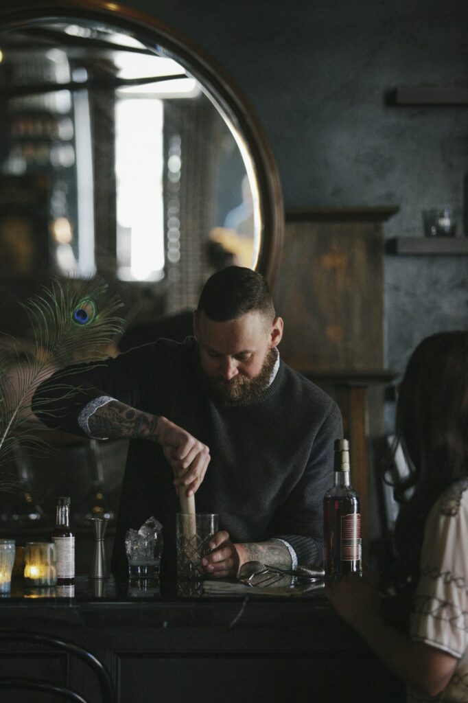A woman and a bartender talking, and mixing drinks.
